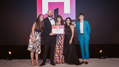 Five people standing together on a stage; one in the center holds a framed certificate.